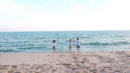 Young  asian girl holds her friends hand running into the sea, friends having fun in sea waves at beach, enjoying with travel and resting on summer vacation or holiday concept.の写真素材