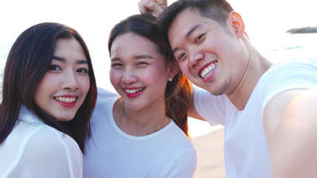 Group of happy young adult friends taking selfies on smartphone on a beach at sunset ,Group of happy friends spending time together at the beach on summer holidays, friendship, happy summer holidays.の写真素材
