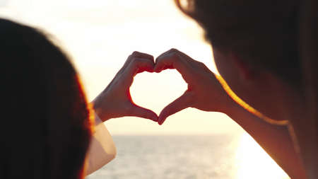 Happy young couple in love making heart shape with fingers on the beach sunset, romantic relationships in vacation holidays, enjoying with travel and resting on summer vacation or holiday concept.の写真素材
