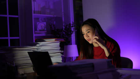 Young asian woman calling with customer her sitting work overtime doing late time business at office in night on desk, Businesswoman concept.の写真素材