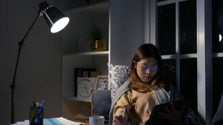 Asian businesswoman or freelancer working hard at the night looking the laptop digital tablet and document in workplace at late overtime deadline, Stressed busy and exhausted of work at home.の写真素材