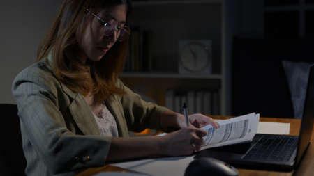 Asian businesswoman or freelancer working hard at the night looking the laptop digital tablet and document in workplace at late overtime deadline, Stressed busy and exhausted of work at home.の写真素材