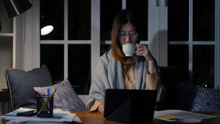 Asian businesswoman or freelancer working hard at the night looking the laptop digital tablet and document in workplace at late overtime deadline, Stressed busy and exhausted of work at home.の写真素材