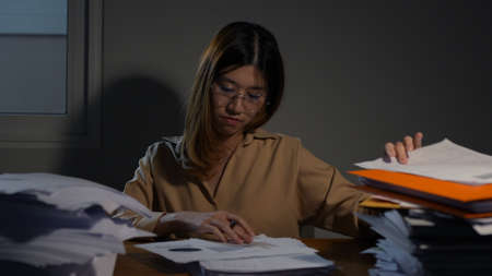 Asian businesswoman or freelancer working hard at the night looking the laptop digital tablet and document in workplace at late overtime deadline, Stressed busy and exhausted of work at home.の写真素材