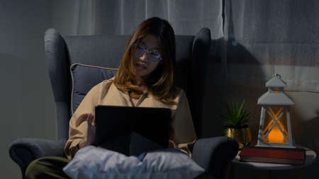 Asian businesswoman or freelancer working hard at the night looking the laptop digital tablet and document in workplace at late overtime deadline, Stressed busy and exhausted of work at home.の写真素材