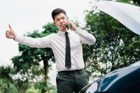 Asian businessman use mobile phone, smart phone after work walking through city street while waiting...