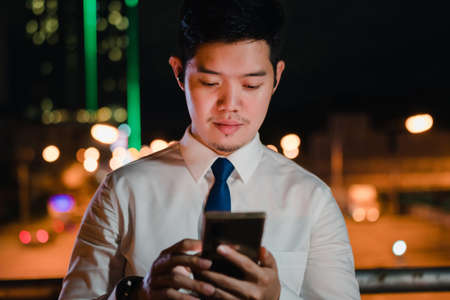 Asian businessman use wireless earbuds listening music in the modern city at nightの写真素材