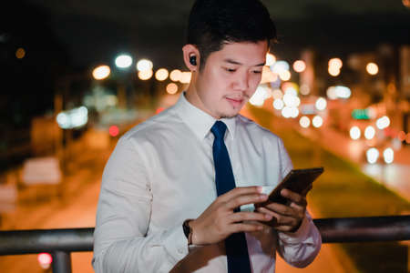 Asian businessman use mobile phone, smart phone after work walking through city street while waiting...