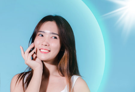 Smiling asian beauty woman hold sun cream with sun protection uv or sunscreen, sun block on the blue backgroundの写真素材