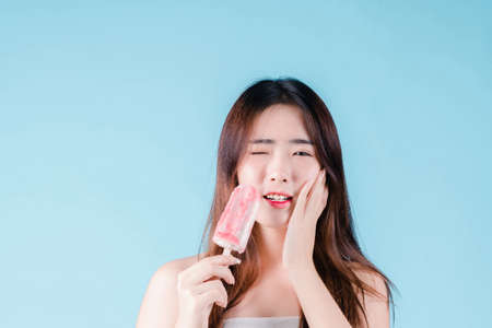 Asian woman hold have a hypersensitive teeth on the blue backgroundの写真素材