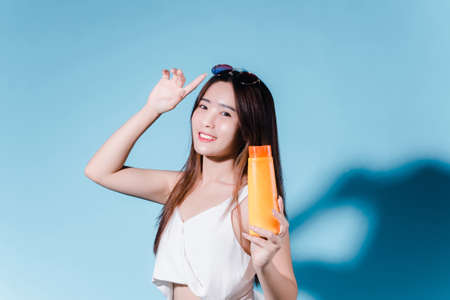 Charming asian beauty woman hold sun cream with sun protection uv or sunscreen on the blue backgroundの写真素材