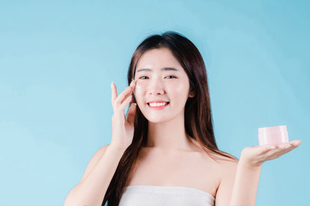 Asian beauty woman applying moisturizer, lotion, serum on facial by skin care on the blue backgroundの写真素材