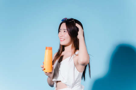 Charming asian beauty woman hold sun cream with sun protection uv or sunscreen on the blue backgroundの写真素材
