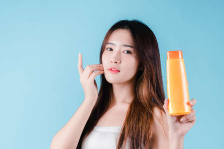 Charming asian beauty woman hold sun cream with sun protection uv or sunscreen on the blue backgroundの写真素材