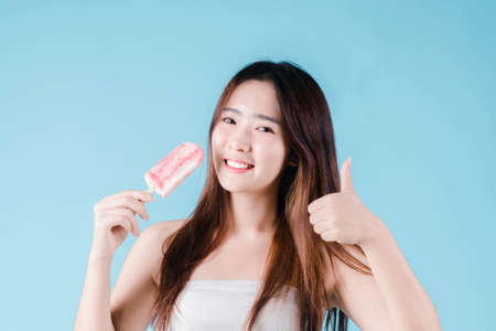 Asian woman hold and show ok gesture have strong teeth on the blue backgroundの写真素材