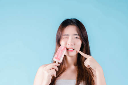 Asian woman hold have a hypersensitive teeth on the blue backgroundの写真素材