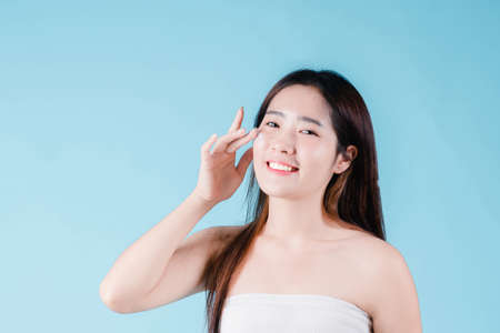 Asian beauty woman applying moisturizer, lotion, serum on facial by skin care on the blue backgroundの写真素材