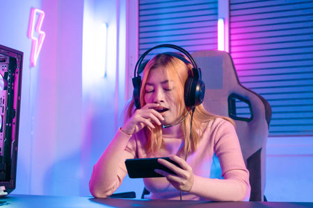 A Professional female pro gamer play online mobile games smartphone cyber sport and esport yawn, bored emotion. Young woman in tournament match worldwide in room colorful neon lights.の写真素材