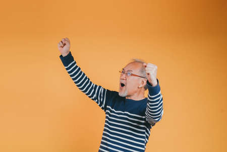 Excited glad expression of Senior elderly old man arms raised to celebrating victory success feeling, Happy Asian elder man with glasses yes like winner emotion on yellow backgroundの写真素材