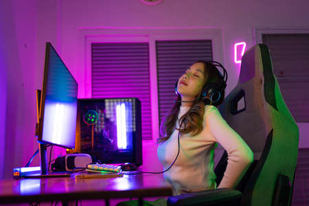 Young people Backache. Gamer and E-Sport online of Asian woman playing online computer video game with lighting effect, broadcast streaming live at home. She a backache due to sitting for a long timeの写真素材