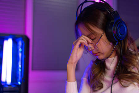 Eyes tired. Gamer and E-Sport online of Asian woman playing online computer video game with lighting effect, broadcast streaming. Her eyes were tired from staring at the screen for a long time.の写真素材
