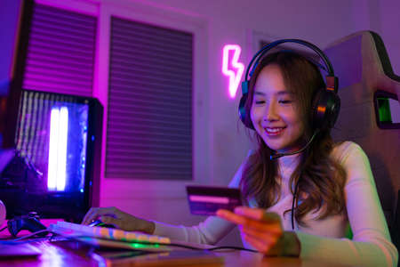 Top up online game with credit card concept. Gamer and E-Sport online of Asian woman playing online computer video game with lighting effect, broadcast streaming live at home. Gamer and E-Sport gamingの写真素材