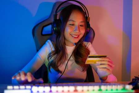 Top up online game with credit card concept. Gamer and E-Sport online of Asian woman playing online computer video game with lighting effect, broadcast streaming live at home. Gamer and E-Sport gamingの写真素材