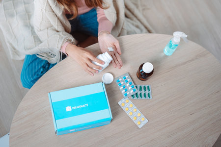 Asian young woman patient on eating table at nursing home care. Female look to medicine pills in bottle, read prescription and content. self recover health care concept.の写真素材