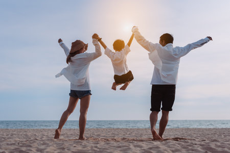 Happy asian family jumping together on the beach in holiday vacation. Silhouette of the family holding hands enjoying the sunset on the sea beach. Happy family travel, trip  family holidays weekend.の写真素材