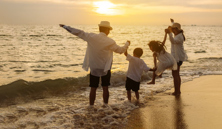 Happy asian family jumping together on the beach in holiday vacation. Silhouette of the family holding hands enjoying the sunset on the sea beach. Happy family travel, trip  family holidays weekend.の写真素材