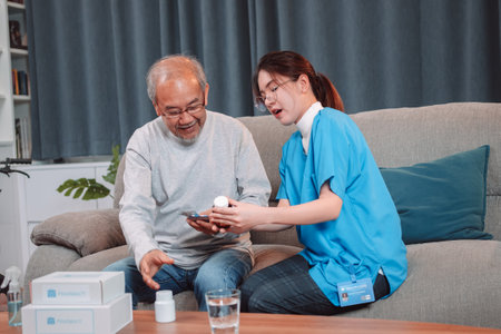 Asian senior male patient consult prescription drug with physician nurse at nursing home. Caregiver therapist pharmacist woman hold medicine pills bottle, medicine dosage at house in living room.の写真素材