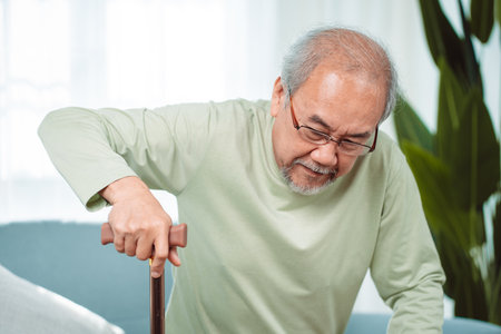 Asian Senior elderly old man disabled patient walking slowly his use walker or cane in living room at home. Feeling painful and suffering from knee pain. Healthcare medical and insurance conceptの写真素材