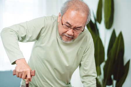 Asian Senior elderly old man disabled patient walking slowly his use walker or cane in living room at home. Feeling painful and suffering from knee pain. Healthcare medical and insurance conceptの写真素材