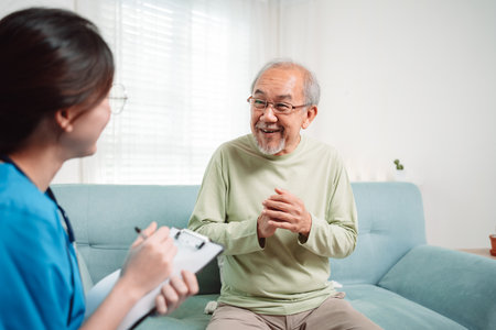 Asian caregiver talking senior male patient checkup in living room at home. Older elderly man consults after physical therapy. Nurse assistance rescue concept.の写真素材