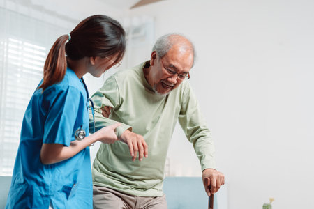 Asian senior elderly man patient doing physical therapy with caregiver. woman nurse helping get up from wheelchair for practice walking with walker at home, practice walk slowly at nursing home care.の写真素材