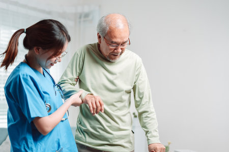 Asian senior elderly man patient doing physical therapy with caregiver. woman nurse helping get up from wheelchair for practice walking with walker at home, practice walk slowly at nursing home care.の写真素材