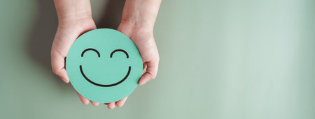 Hands holding green happy smile face, good feedback rating, positive customer review, experience, satisfaction survey, smiley mental health, child wellness, world mental health day on green backgroundの写真素材