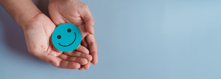 Hands holding blue happy smile face, good feedback rating, positive customer review, experience, satisfaction survey, smiley mental health, child wellness, world mental health day on blue backgroundの写真素材