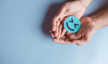 Hands holding blue happy smile face, good feedback rating, positive customer review, experience, satisfaction survey, smiley mental health, child wellness, world mental health day on blue backgroundの写真素材