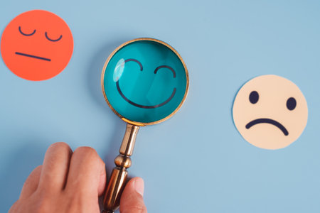 Hand holding magnifier focus selected happy smiley face paper cut which is among various emotions, good feedback rating and positive customer review, experience, satisfaction survey, mental healthの写真素材