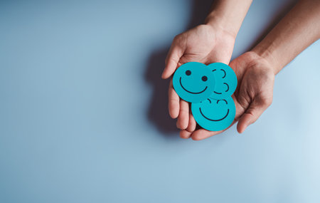 Hands holding blue happy smile face, good feedback rating, positive customer review, experience, satisfaction survey, smiley mental health, child wellness, world mental health day on blue backgroundの写真素材