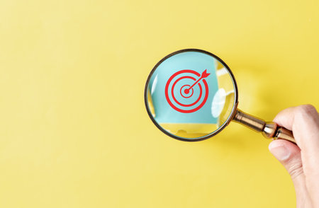 Dartboard with arrow hiding of yellow punched paper, hand holding magnifying discovery target for planning business objective target to successful development, innovation, idea, creative.の写真素材