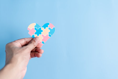 Hand holding Awareness heart jigsaw puzzle, Color puzzle symbol of awareness for autism spectrum disorder family support. Autism World Awareness Day.の写真素材