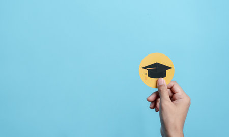Hand holding education cap paper cut, leading to success goal. Taking strategic steps towards...