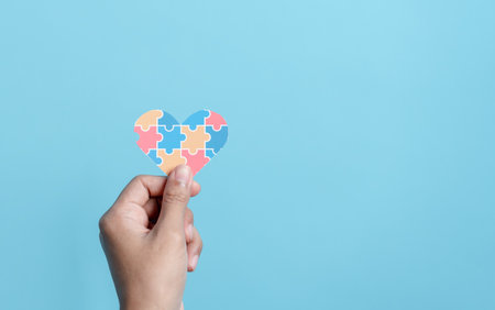 Hand holding Awareness heart jigsaw puzzle, Color puzzle symbol of awareness for autism spectrum disorder family support. Autism World Awareness Day.の写真素材