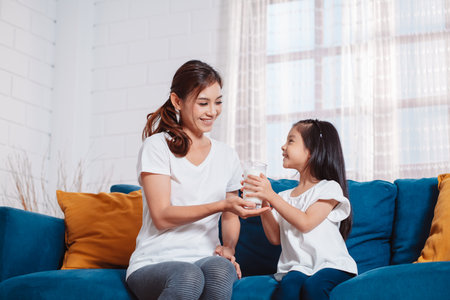 Mother give a glass of milk to lovely daughter, drinking milk at home to nourish healthy vitamins and strong teeth.の写真素材