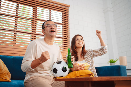 Asian Couple watching sport football cheering excited on sofa in living room at home. enjoy relaxing happiness.の写真素材