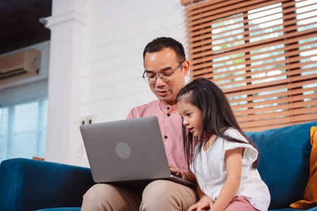 Cute little asian daughter with father working on laptop at home. single loving dad man shopping insurance to daughter by online technology.の写真素材