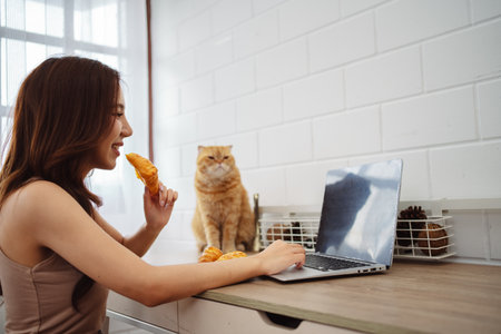 Happy asian young woman working with laptop computer with cute cat in the morning daytime.の写真素材