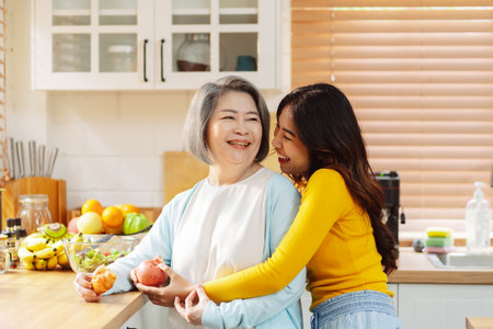 Happy asian woman daughter hugging senior mother in the kitchen room eating healthy food happy enjoying.の写真素材